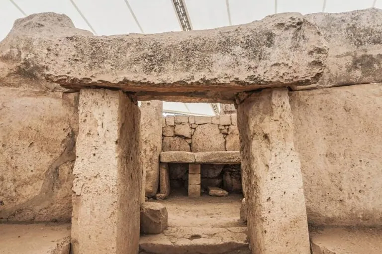 Ancient stone structure with large rectangular slabs forming doorway and walls, under a protective canopy.