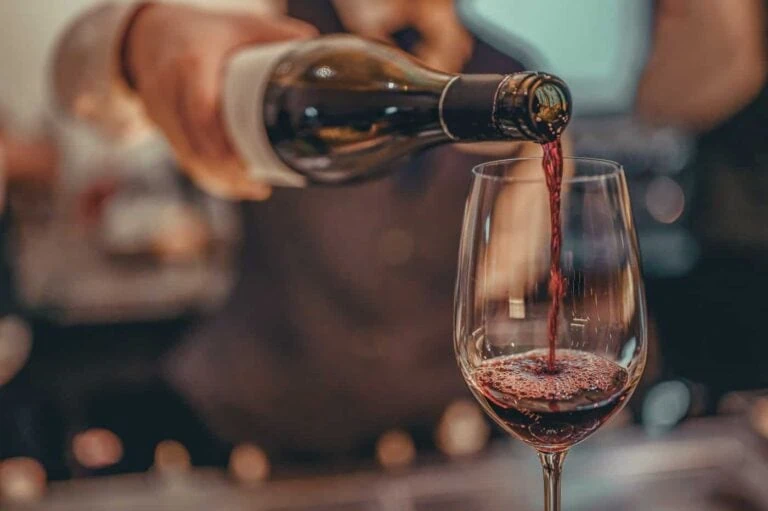 Red wine being poured from a bottle into a wine glass, with a blurred background.