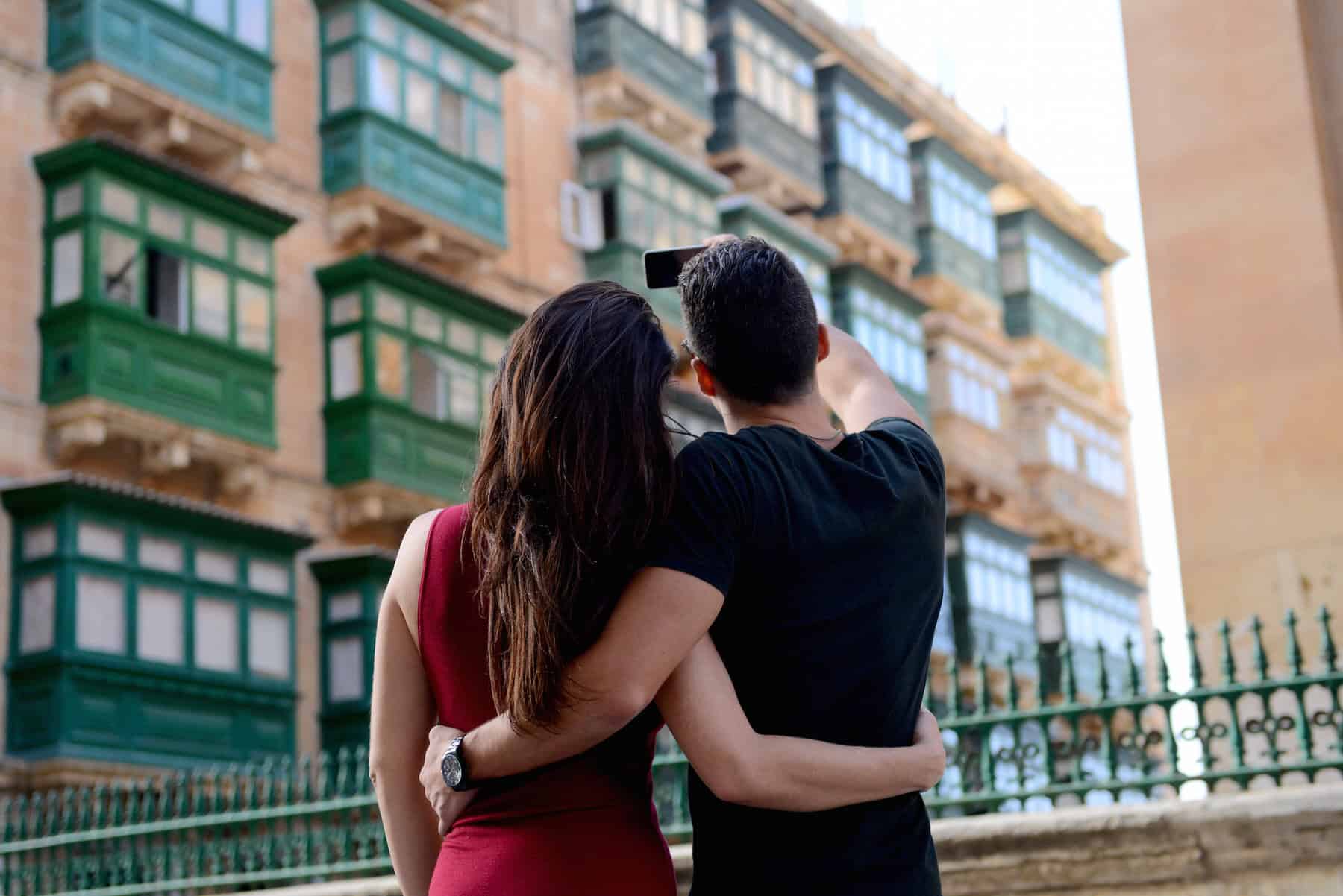 A couple takes a selfie in front of a building with green balconies.