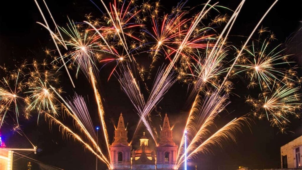 Colorful fireworks burst over a historical church at night, illuminating the sky with vibrant streaks and patterns.