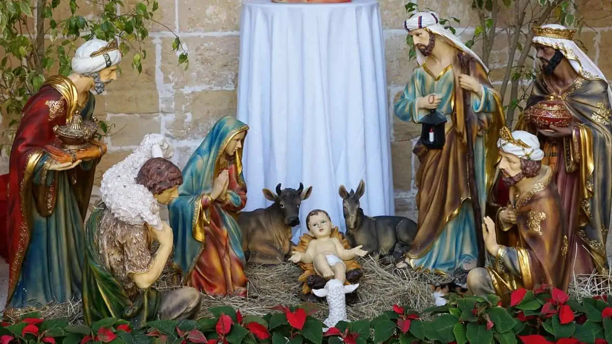 Nativity scene with figurines of baby Jesus, Mary, Joseph, wise men, shepherd, animals, and greenery on straw.