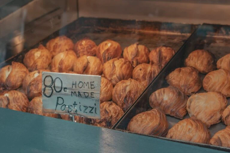 A display of Malta's traditional food, pastizzi pastries, sits enticingly in a glass case, accompanied by a handwritten sign reading "80c homemade pastizzi.