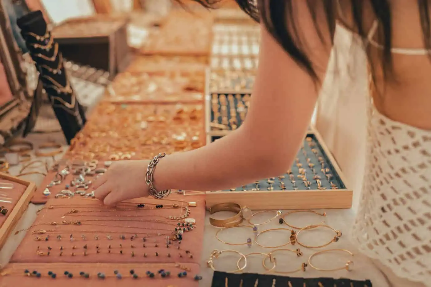 Amidst a scene reminiscent of atmospheric churches in Malta, a person carefully selects jewelry from a display table teeming with exquisite rings, bracelets, and necklaces.
