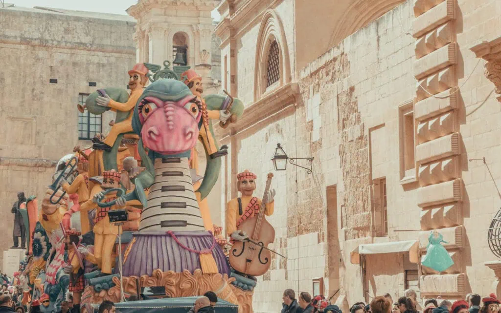 A vibrant parade float featuring musicians and fantasy creatures winds through a historic street, enchanting the spectators with the joyous spirit of Carnival in Malta.