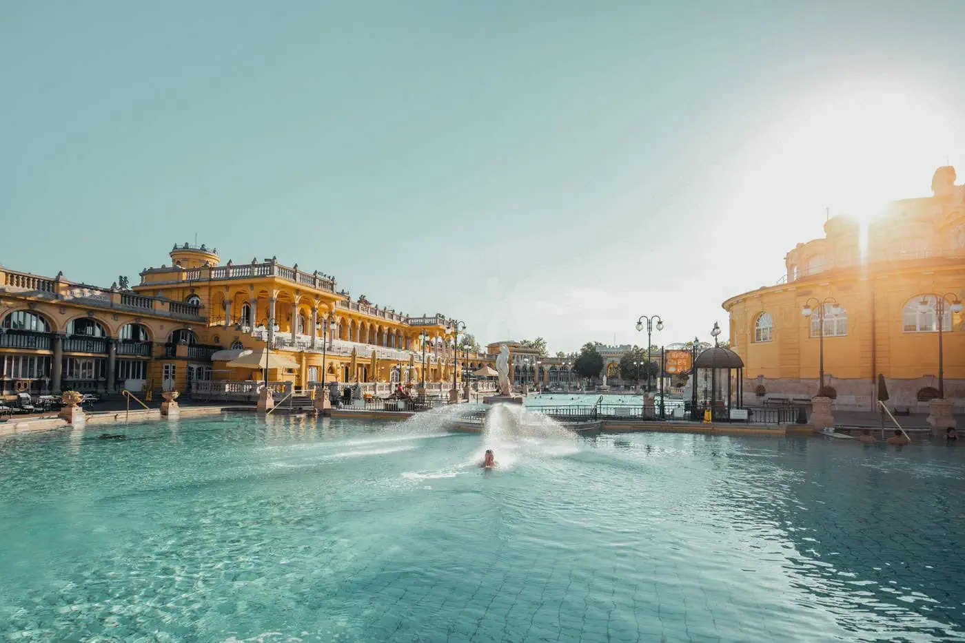 Large ornate outdoor pool with grand yellow buildings in the background, under a bright, clear sky.