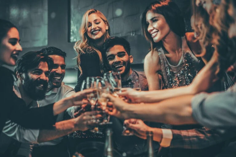 A group of people smiling and clinking glasses in a celebratory manner indoors.