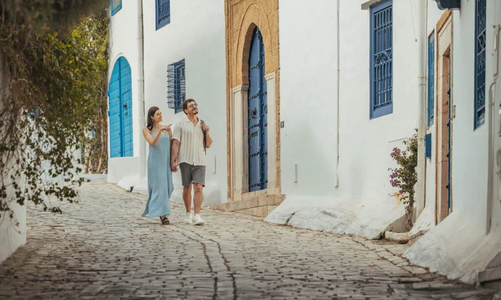 A couple enjoys a leisurely walk along a cobblestone street, immersed in the beauty of their town.