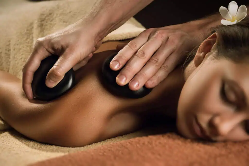 A person receiving a hot stone massage with smooth black stones placed on their back.