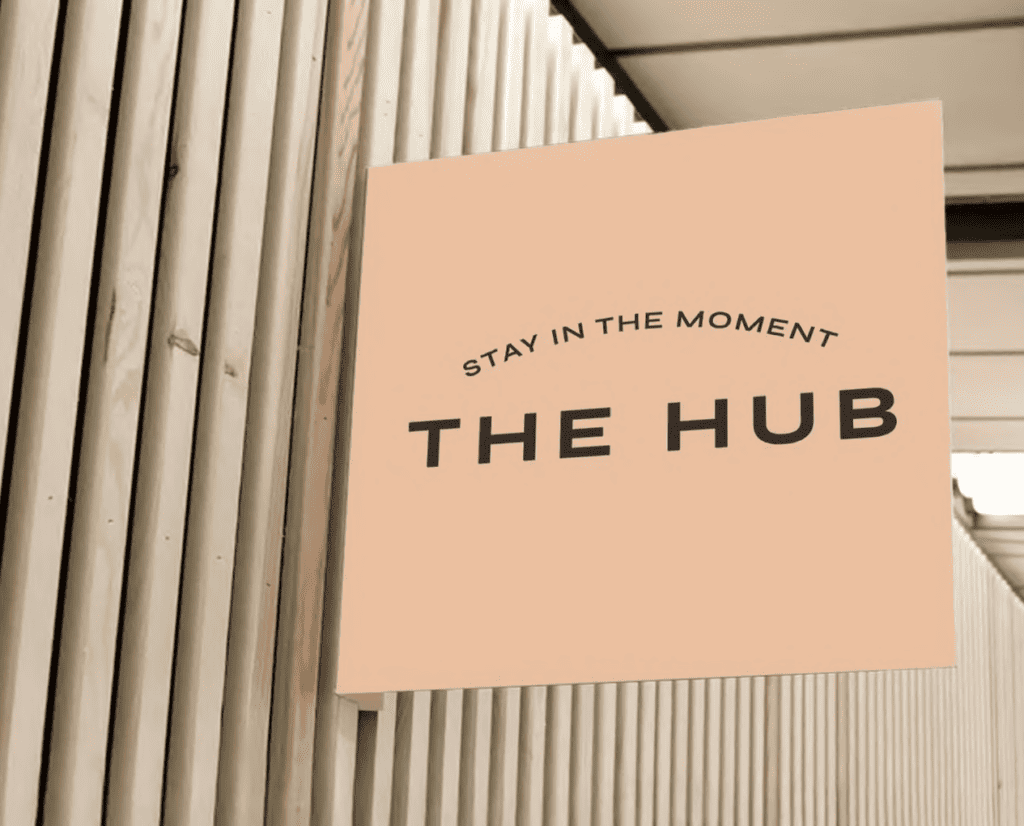 Sign on a wooden wall reads "Stay in the moment, The Hub" in black letters on a peach background.